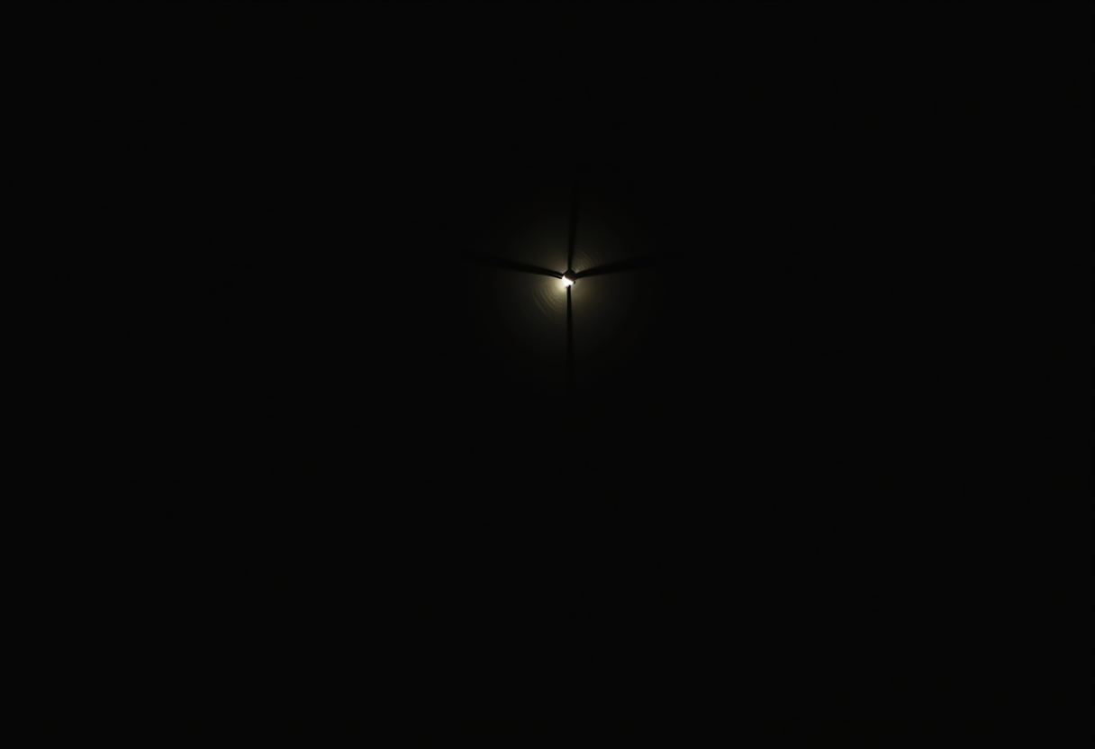 A single small bright light glows at the center of a mostly black frame, with three thin dark blades radiating outward like a windmill silhouette.